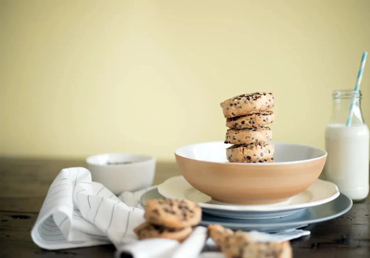 Stapel Schokoladen-Cookies mit Nüssen in Schale, Milchflasche und Tischtuch im Hintergrund.