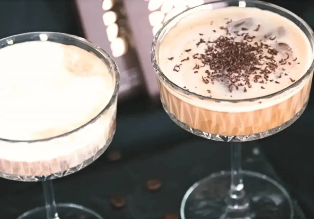 Zwei Gläser mit cremigen Schokoladendesserts, eines mit Schokospänen garniert, auf einer dunklen Unterlage.