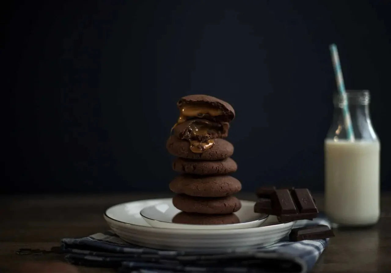Stapel glutenfreier Schokoladen-Cookies mit fließendem Karamellkern, daneben Schokostücke und eine Flasche Milch.