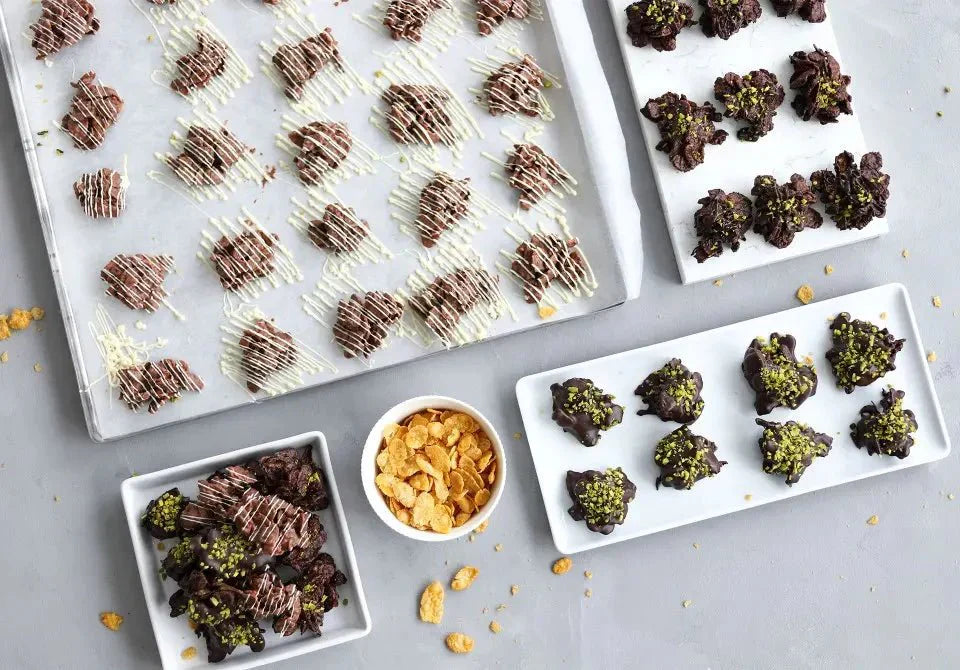 Knusprige Schokoladen-Flakes auf Tabletts mit weißer Schokolade verziert, daneben Cornflakes in einer Schale.