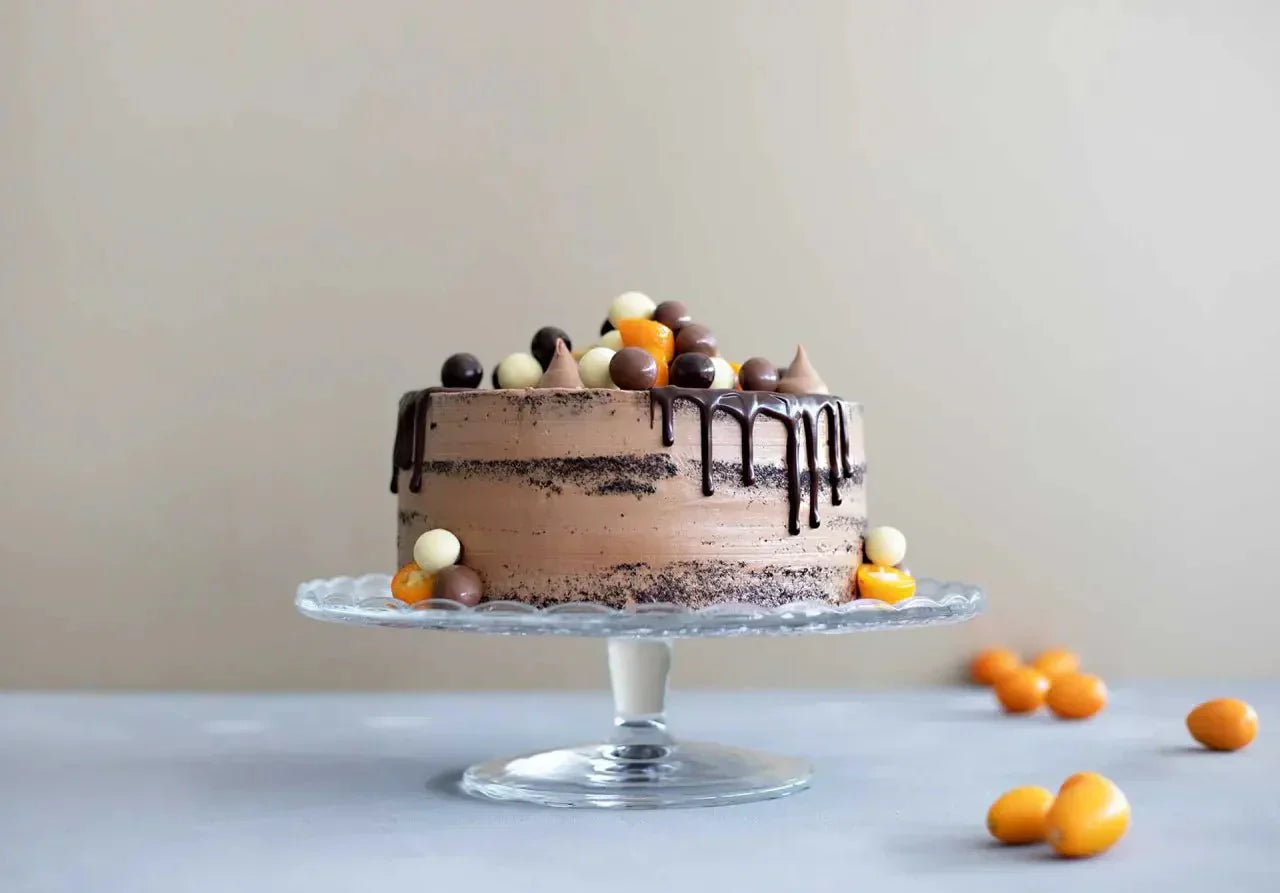 Naked Cake mit Edelako-Schokolade, Schokoglasur und bunten Schokokugeln auf Glasplatte.