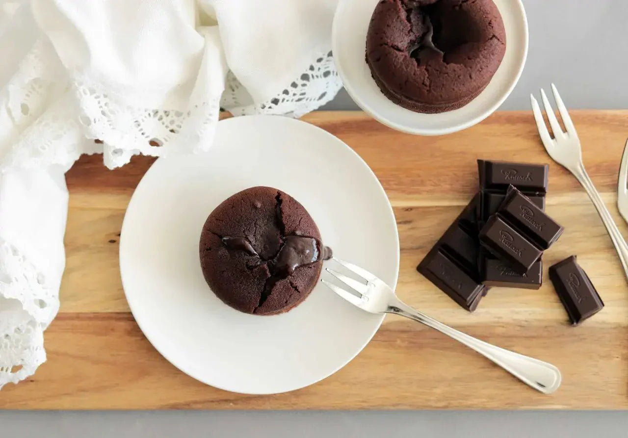 Warmer Schokoladenkuchen mit flüssigem Kern auf weißem Teller, daneben Rausch-Schokoladenstücke und Gabel.