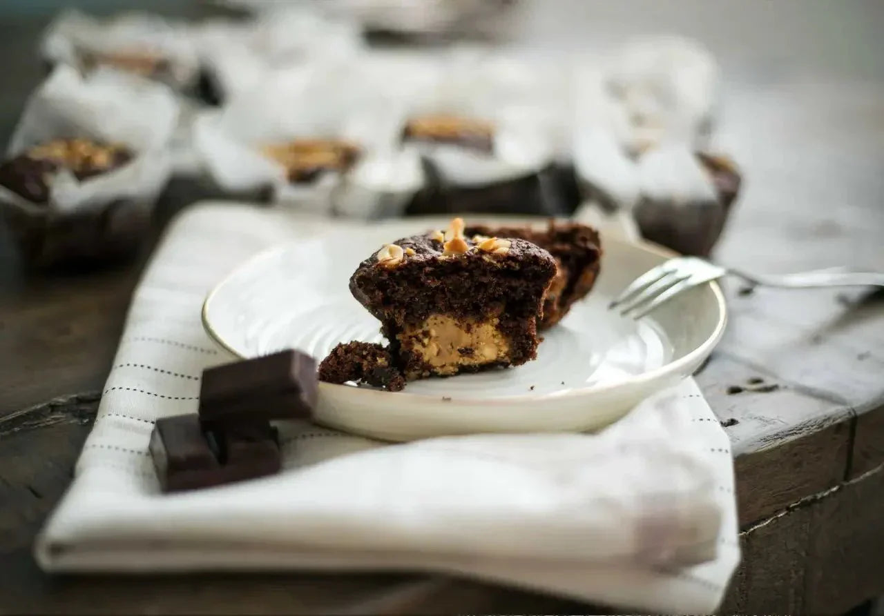 Halb aufgeschnittener Schokoladen-Erdnuss-Muffin auf Teller mit Gabel und Schokoladenstücken im Hintergrund.