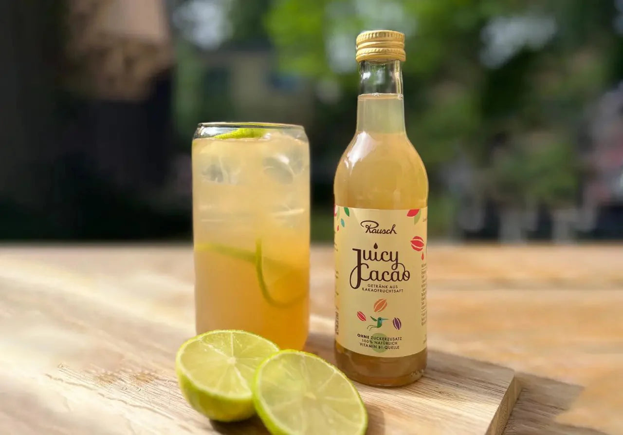 Flasche Juicy Cacao neben einem Cocktailglas mit Limettenscheiben auf einem Holztisch im Freien.