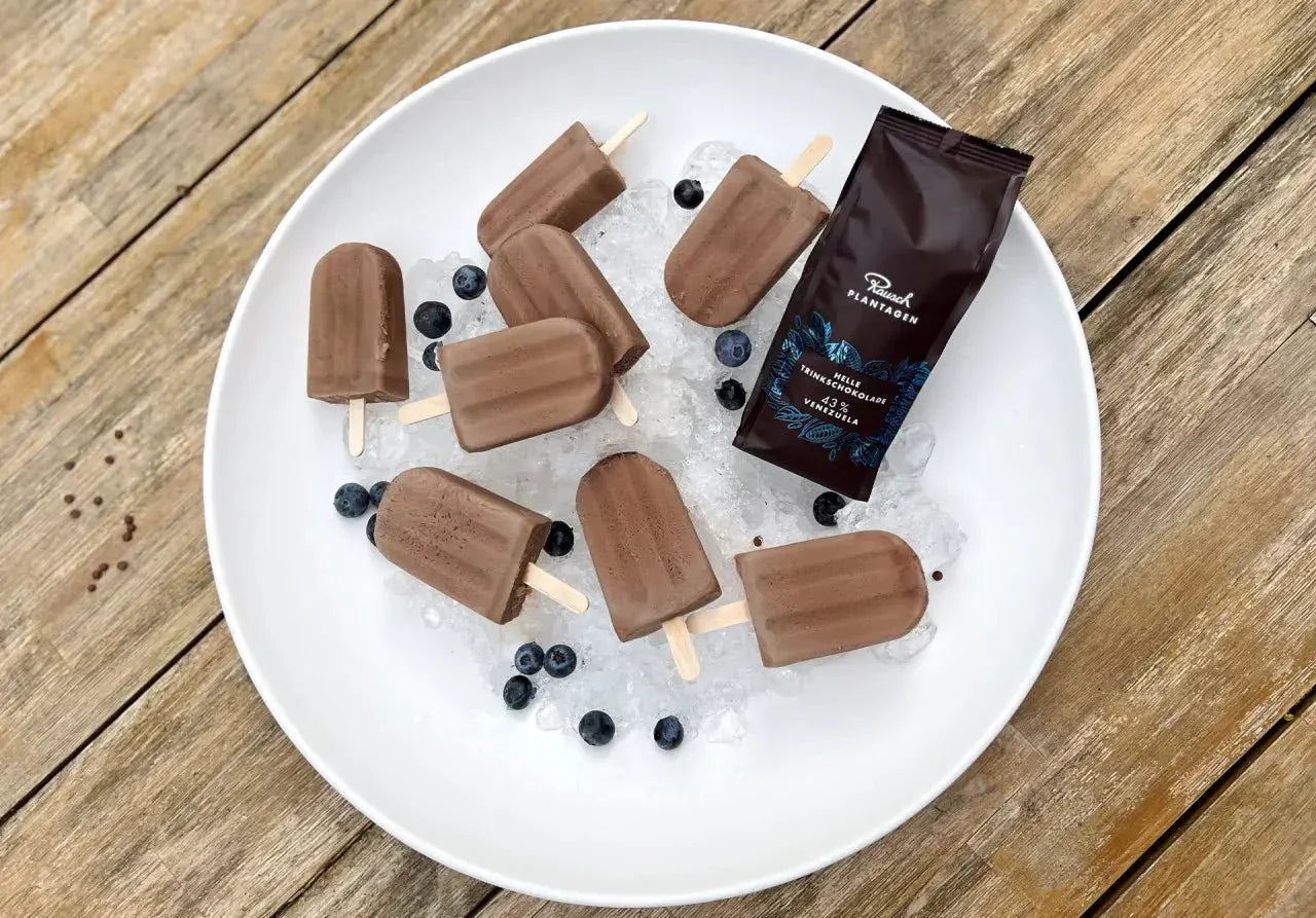 Schokoladen-Eis am Stiel auf Eis in einer weißen Schale, umgeben von Blaubeeren, mit einer Rausch-Schokoladenverpackung.