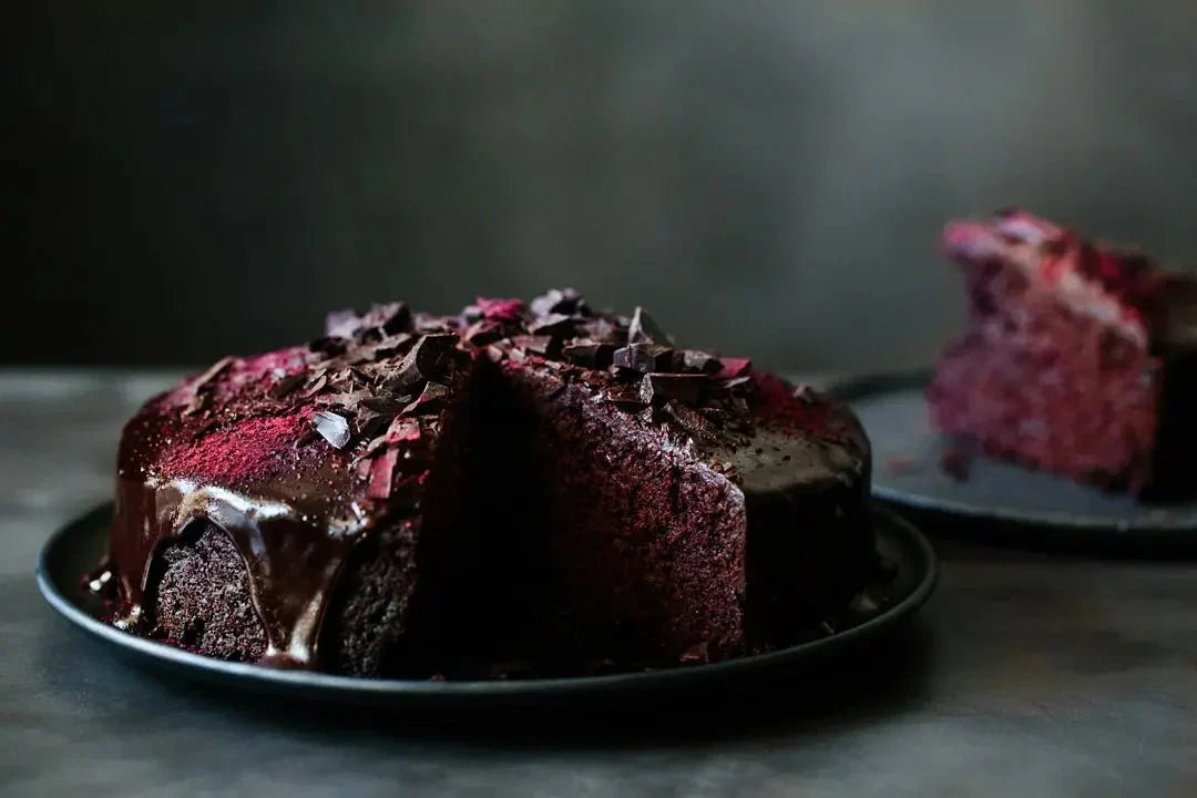 Rote-Bete-Schokoladenkuchen mit dunkler Glasur und Schokoladenstücken auf einem Teller, im Hintergrund weitere Kuchenstücke.