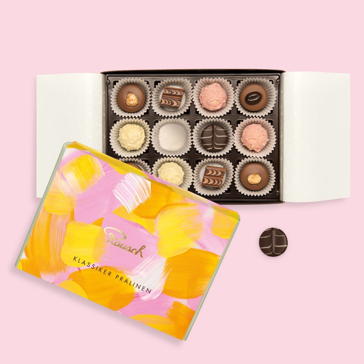 Eine rosa-orange Pralinenschachtel mit Pinselstrich-Muster liegt geöffnet auf rosafarbenem Hintergrund. Im Inneren der Schachtel befinden sich verschiedene Pralinen.