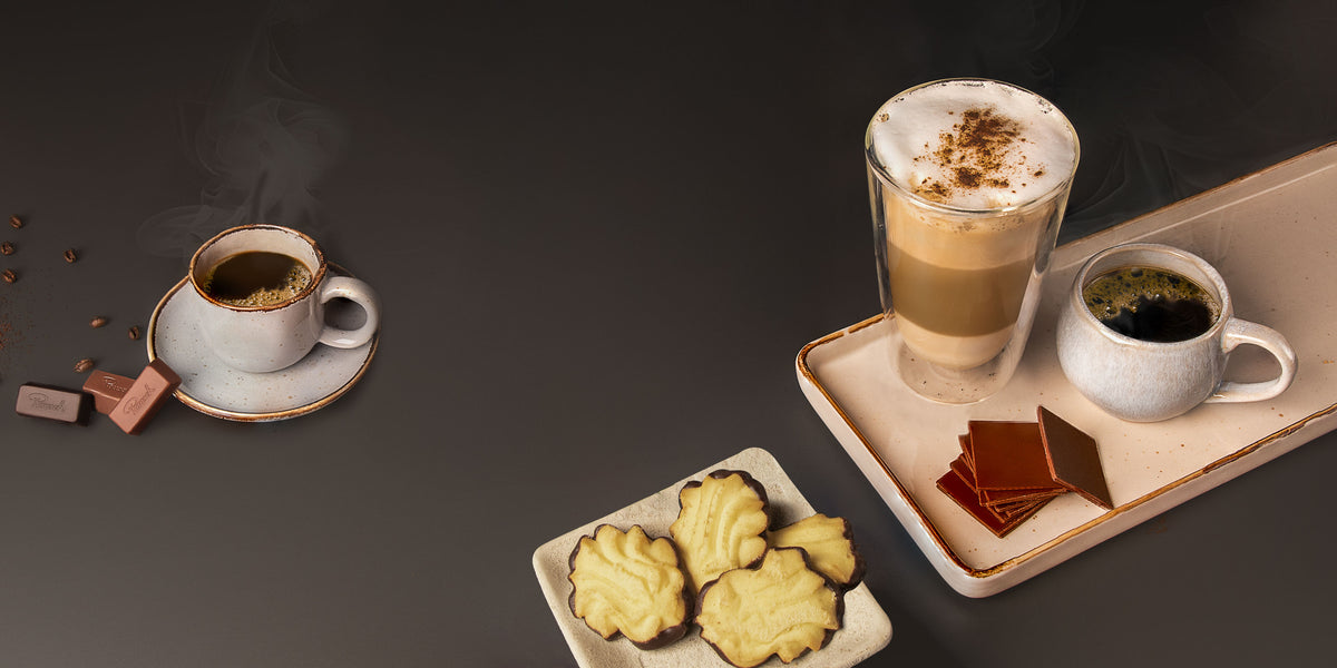 Kaffee und Latte Macchiato auf einem Tisch mit Keksen und Schokolade.