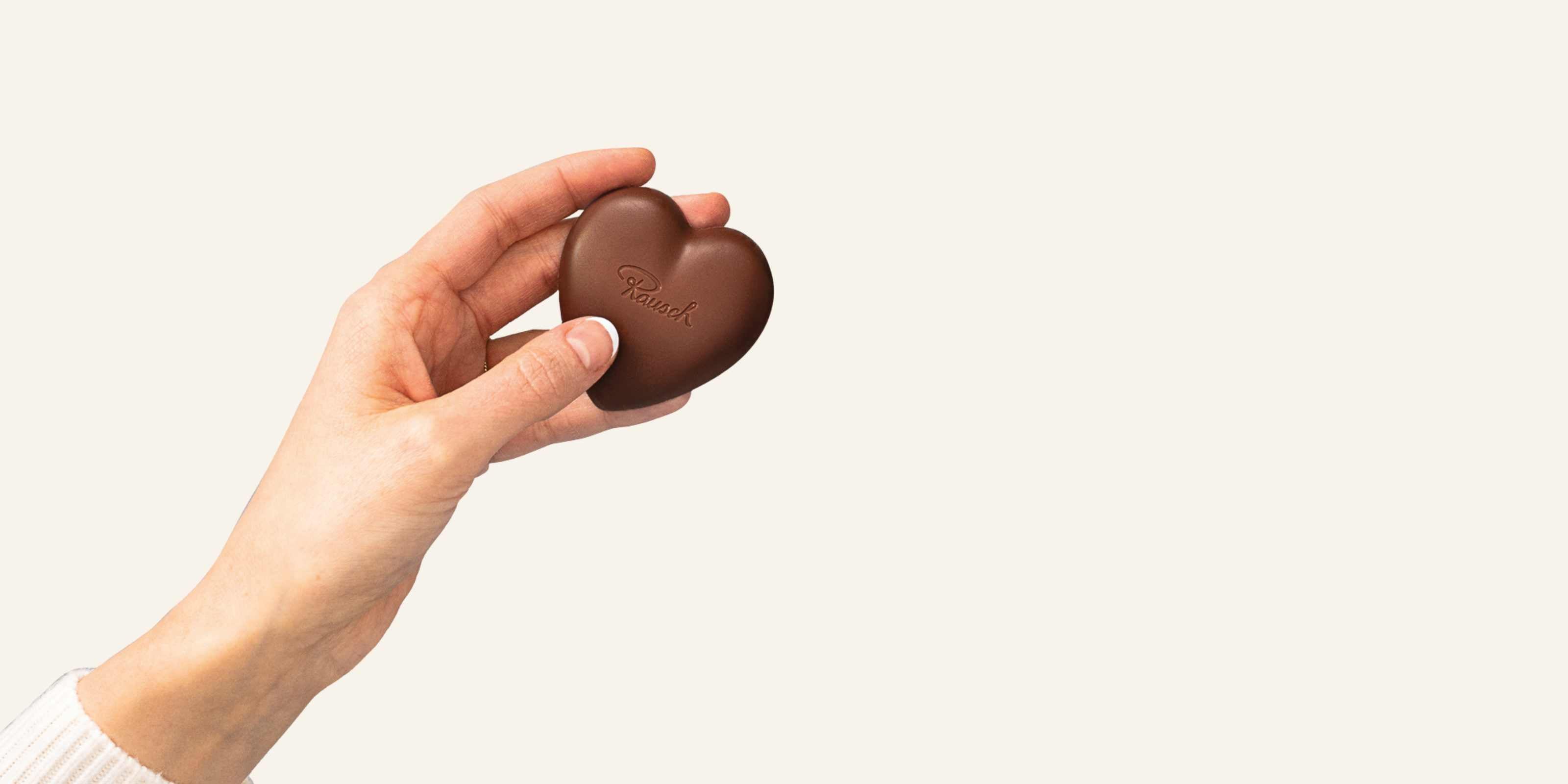 Hand mit Herz aus Schokolade auf beigem Hintergrund