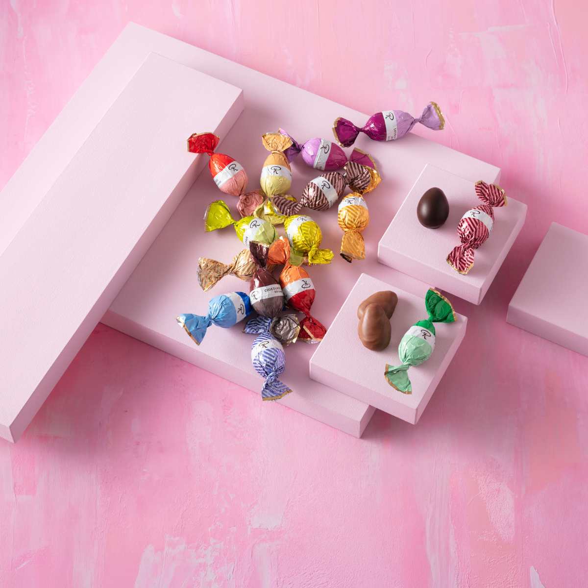 Bunte Pralinen und Schokoladenhasen auf rosa Podesten, Osterdekoration.
