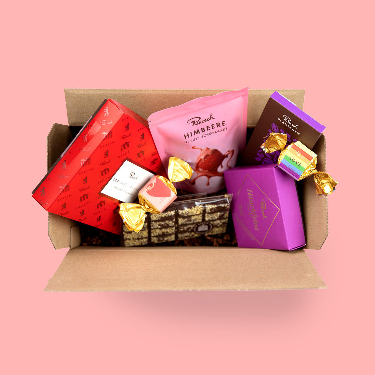 Schachtel mit Rausch Schokoladenprodukten, Himbeere Schokolade, Pralinen und bunte Verpackungen, auf rosa Hintergrund.